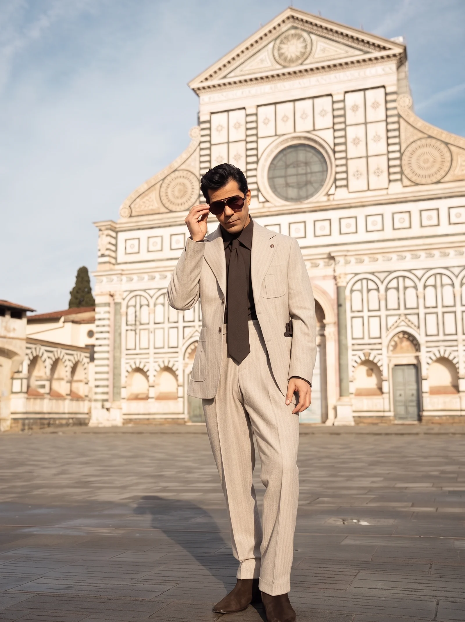 Full-length view of the same model adjusting his sunglasses, with beige suit and dark brown footwear.