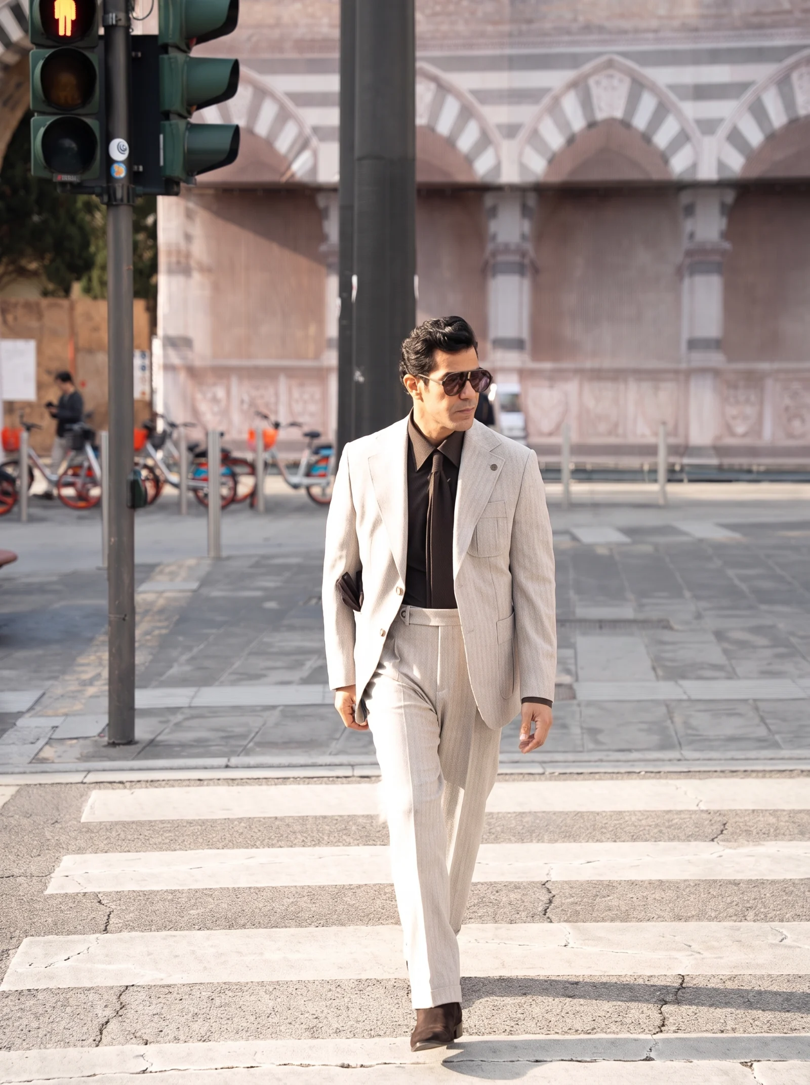 The same model walking across a pedestrian crossing in the beige and brown outfit.